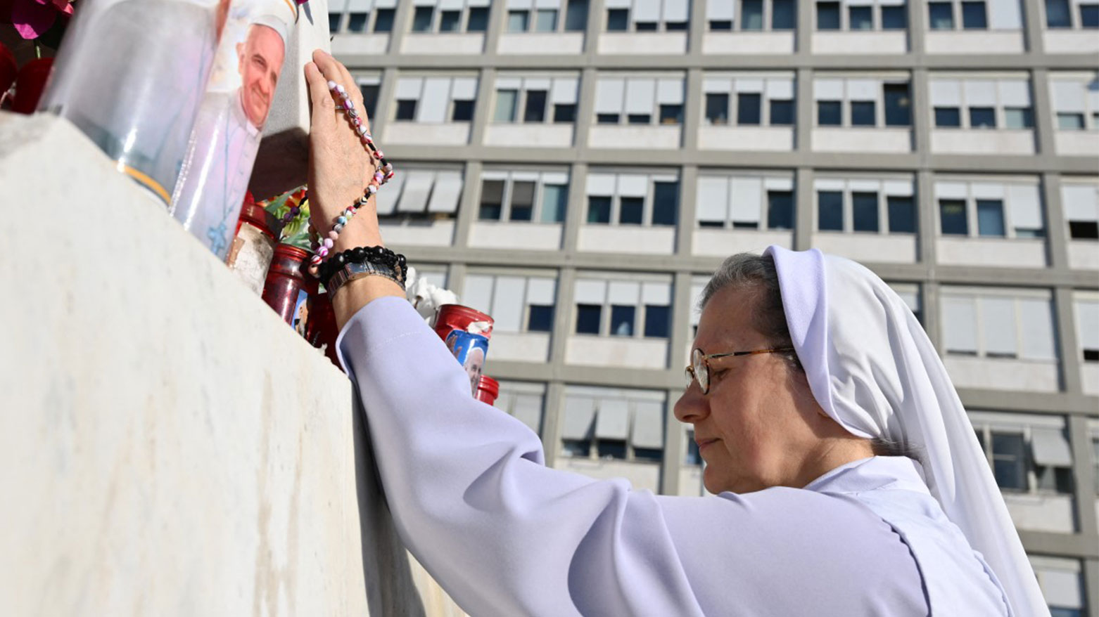 راهبة تصلي عند تمثال البابا يوحنا بولس الثاني خارج مستشفى جيميلي حيث يرقد البابا فرانسيس في روما (فرانس برس)