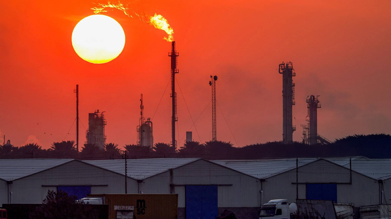 The sun sets behind burning gas flares at the Dora Oil Refinery Complex in Baghdad on Dec. 22, 2024. (Photo: AFP)