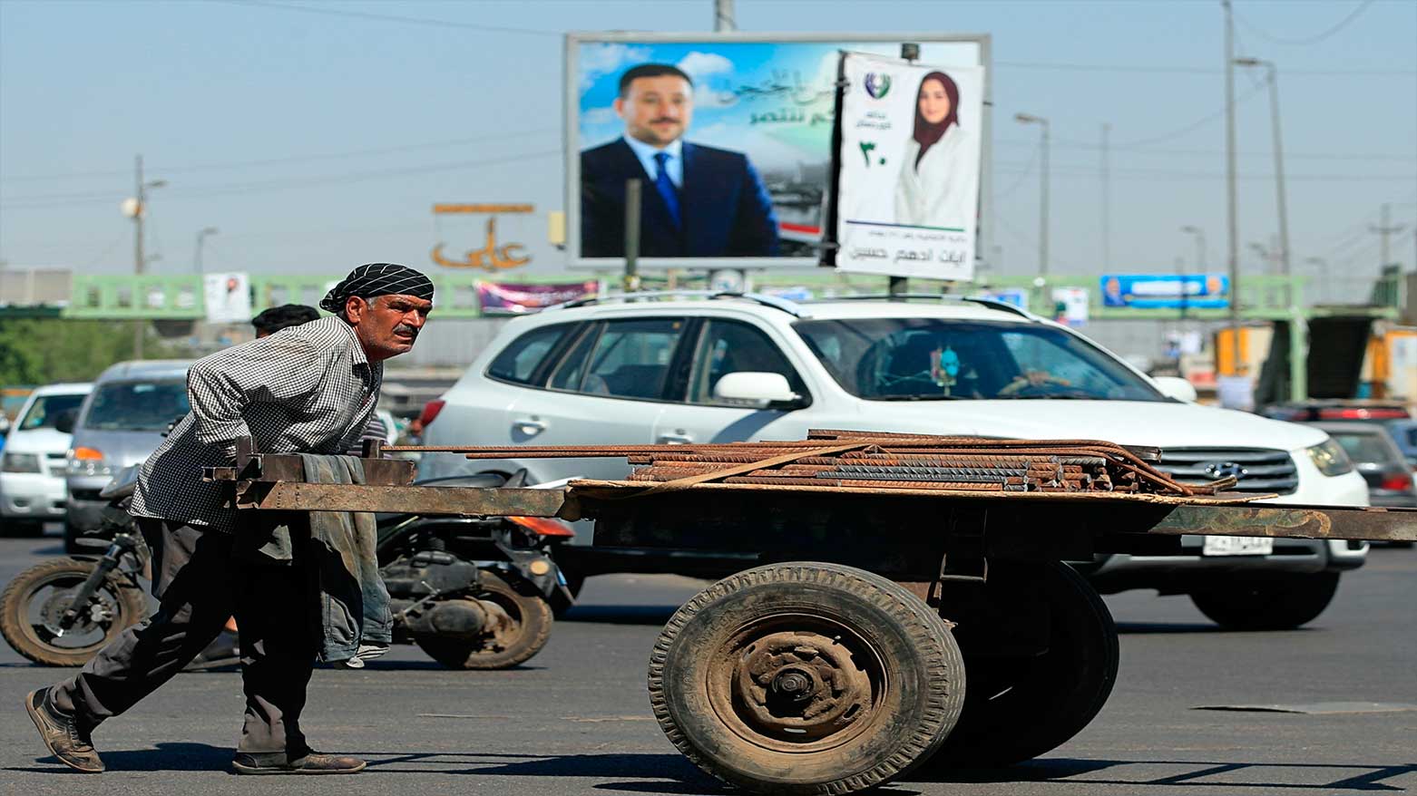 An Iraqi street vendor passes Campaign posters for upcoming parliamentary elections are displayed in Baghdad, Iraq, Oct. 7, 2021. (Photo: AP)