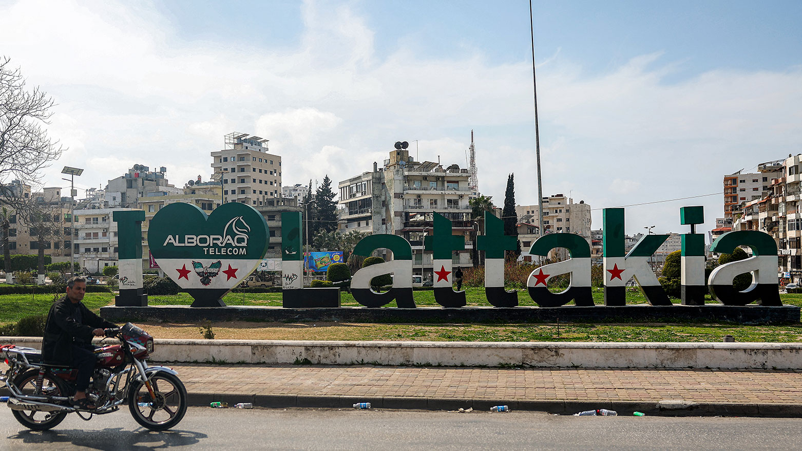 A man rides a motorcycle past a "I love Lattakia" sculpture erected by a telecom shop in a public garden along the side of a road in Syria's western city of Latakia on March 9, 2025. (Photo: AFP)