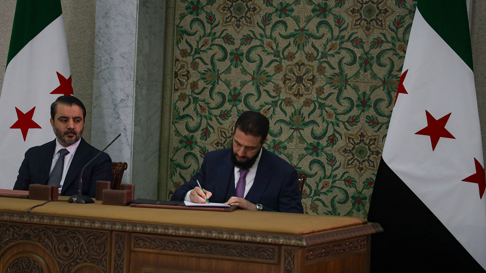 Syria's interim president Ahmad Al-Sharaa, center, signs a temporary constitution for the country in Damascus, Syria, Thursday March 13, 2025. At left foreign minister Asaad Hassan al-Shiban. (Photo: AP)