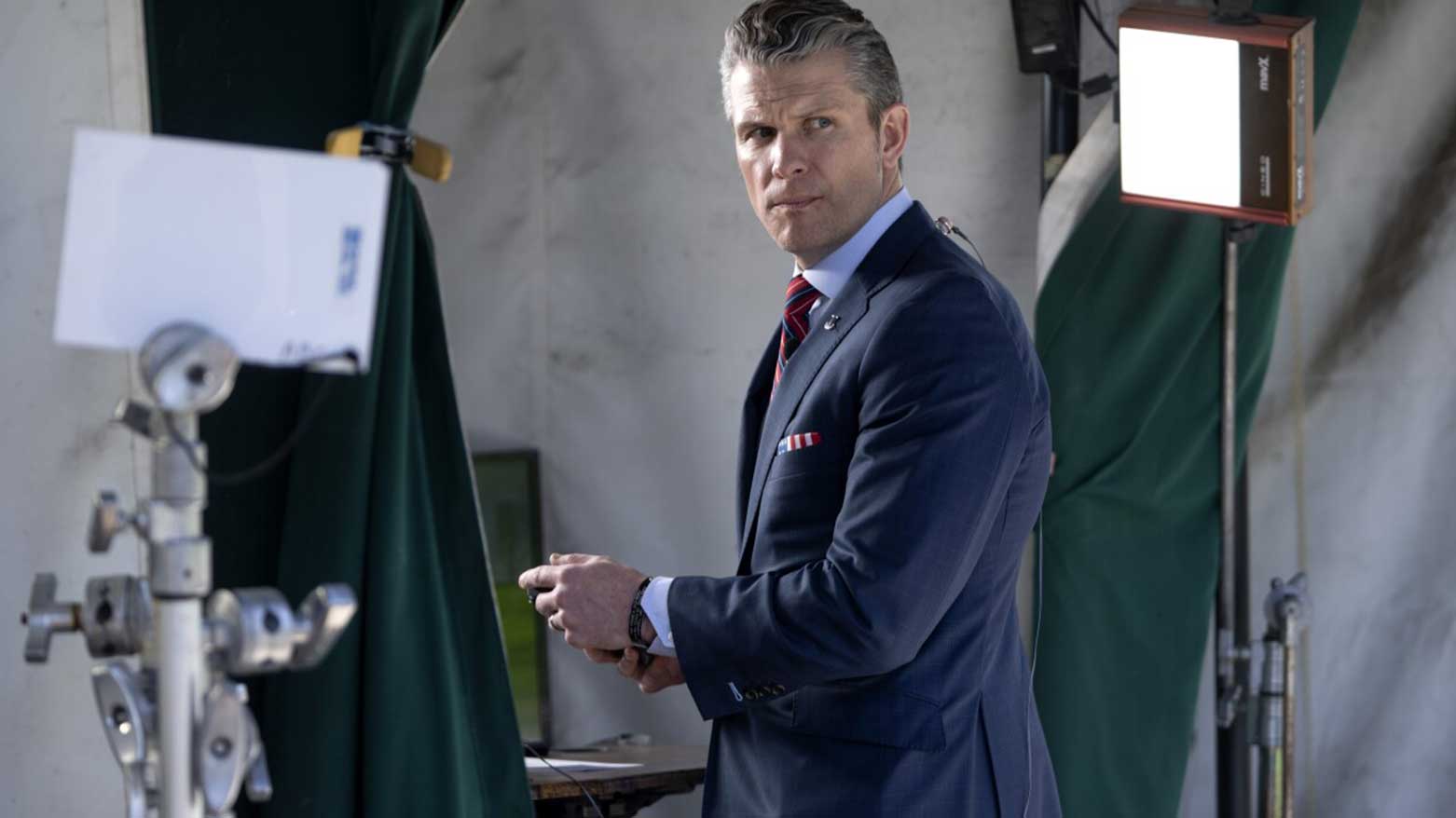 Wearing a U.S. flag themed pocket square and belt buckle, Defense Secretary Pete Hegseth waits for the start of a television interview outside the White House, Friday, March 21, 2025, in Washington. (AP Photo/Jacquelyn Martin)