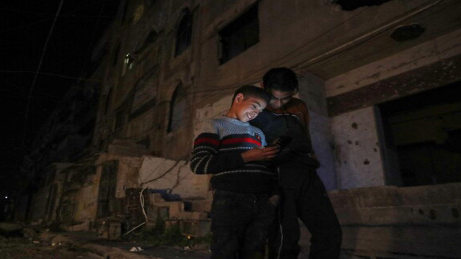 Two boys look at a cellphone in a dark street in Damascus, Syria, early Thursday March 27, 2025. (Photo: AP)