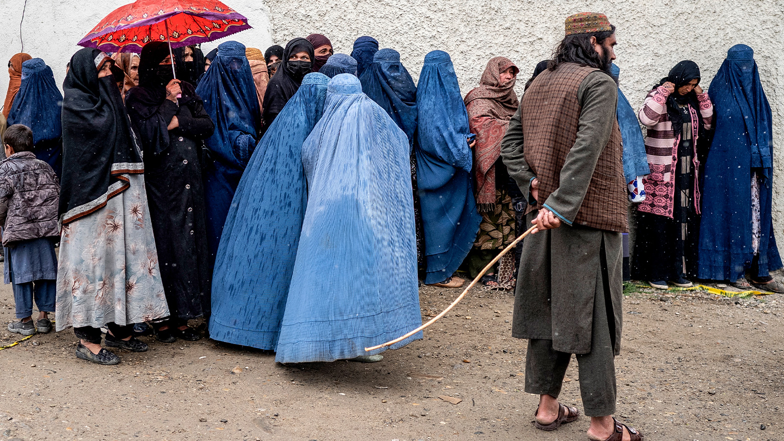 A Taliban security personnel stands guard as Afghan burqa-clad women wait in queue in the midst of a downpour to receive food supplies donated during the Islamic holy fasting month of Ramadan, in Kabul on March 25, 2025. (Photo: AFP)