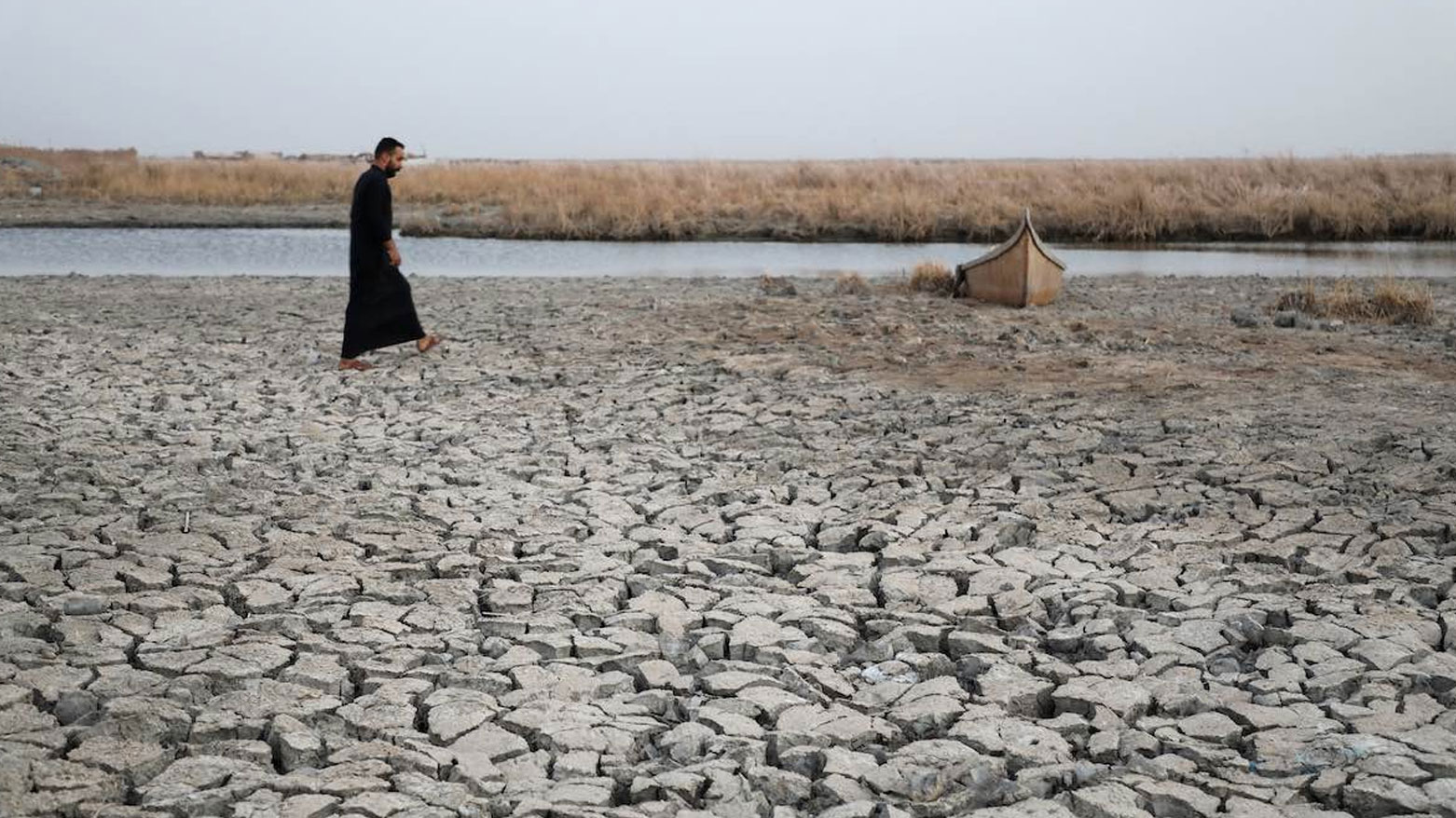 An Iraqi man walking barefoot on cracked, dry land near a river. (Photo: AFP)