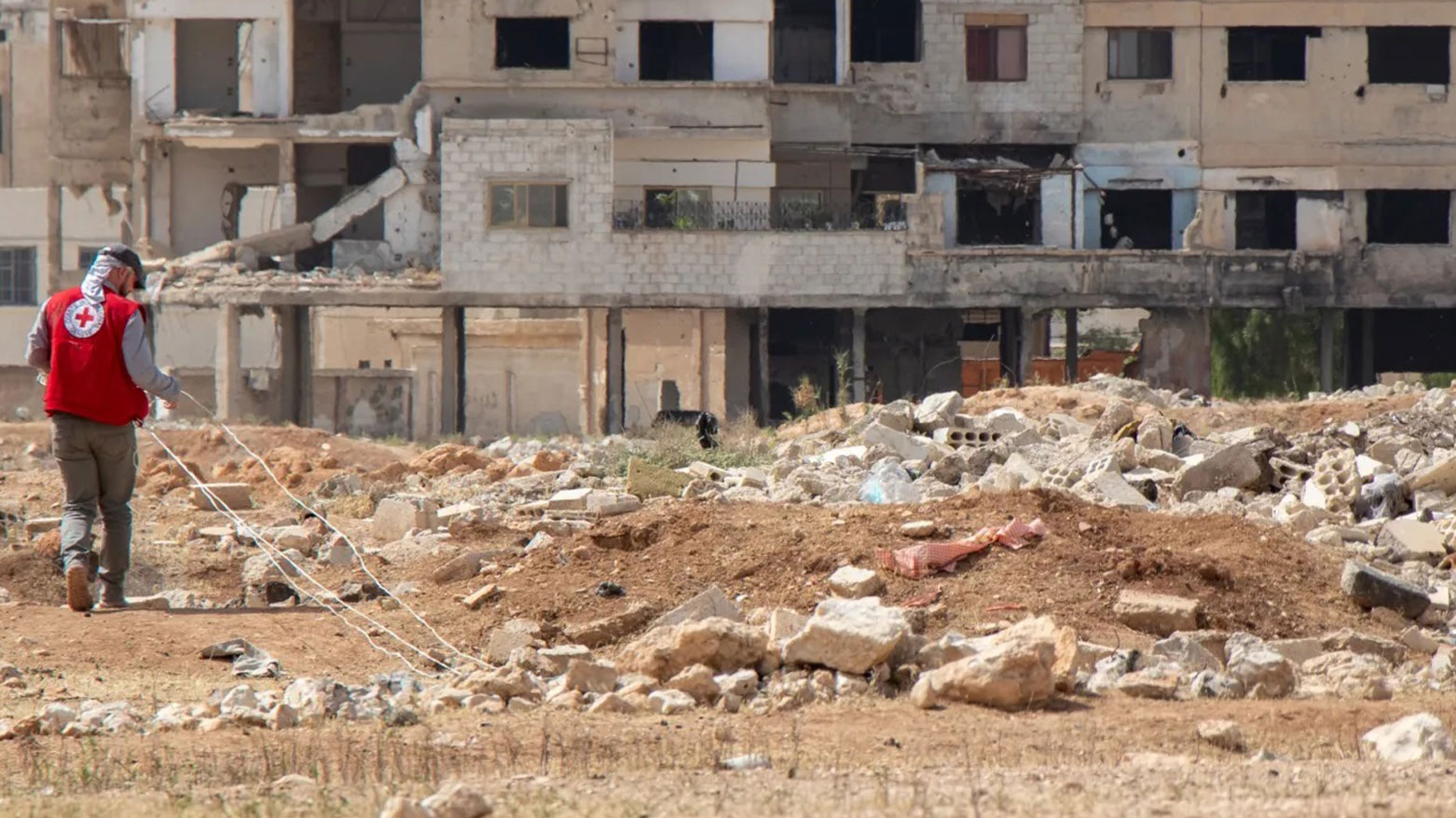 A person wearing a red vest with a Red Cross emblem is working in a rubble-strewn field in Syria. (Photo: ICRC)