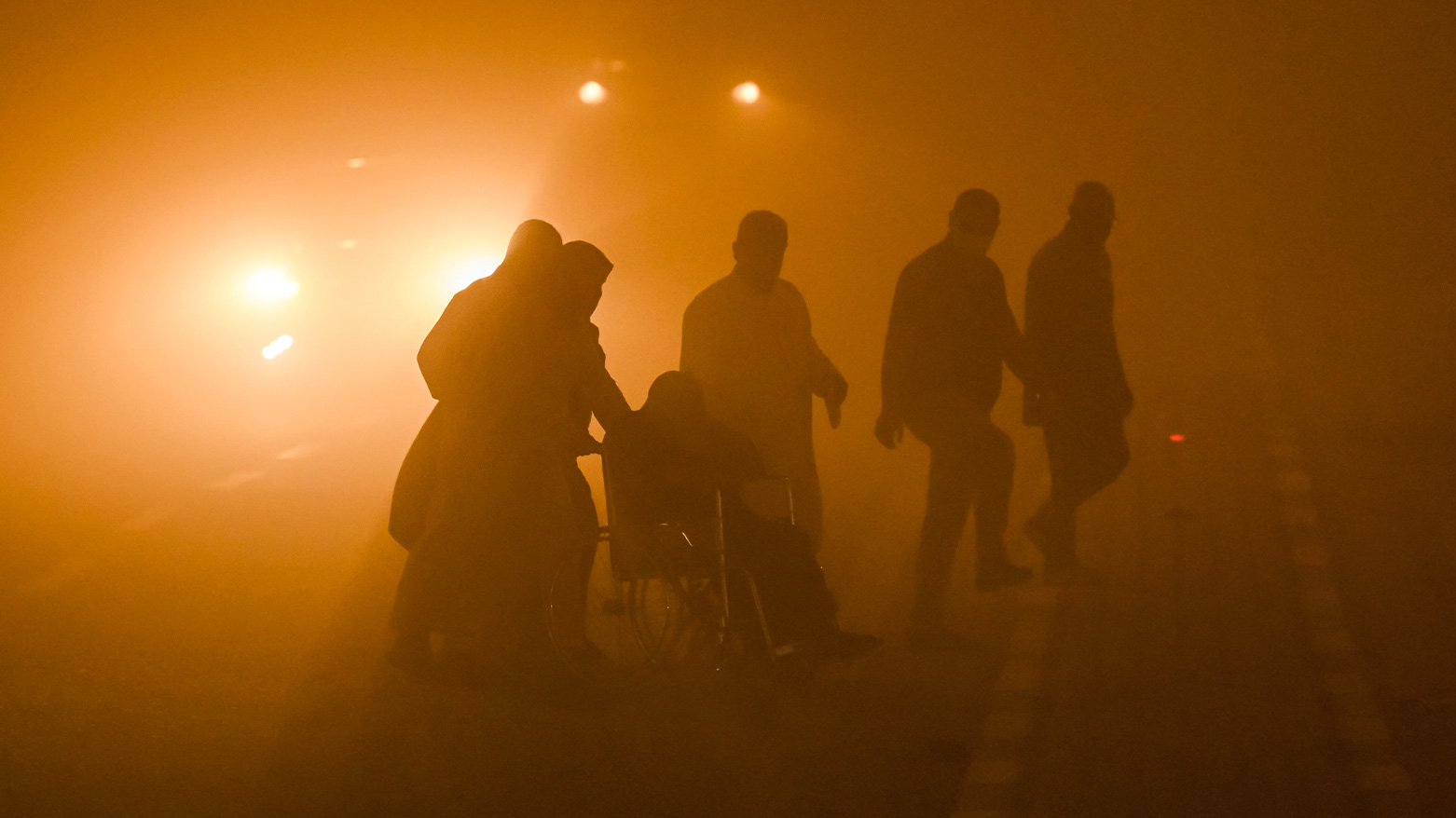 A person in a wheelchair is helped across a road in low visibility during a massive dust storm in Basra. (Photo: AFP)