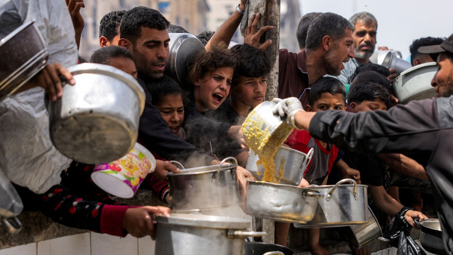 يصطف الناس حاملين أواني الطعام لتلقي وجبات خيرية من مطبخ في بيت لاهيا شمال غزة (فرانس برس)