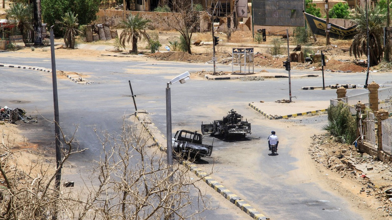 دراجة نارية تقلُ شخصين تسير أمام مركبات عسكرية مدمرة في الخرطوم (فرانس برس)
