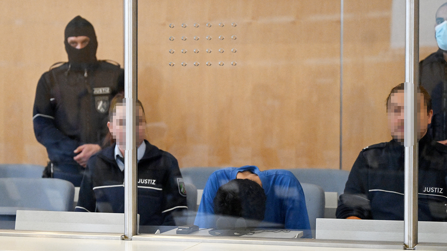 Syrian defendant Issa Al H (C) bends over as he sits next to judicial officers in the dock in the courtroom in Duesseldorf, western Germany, on May 27, 2025,