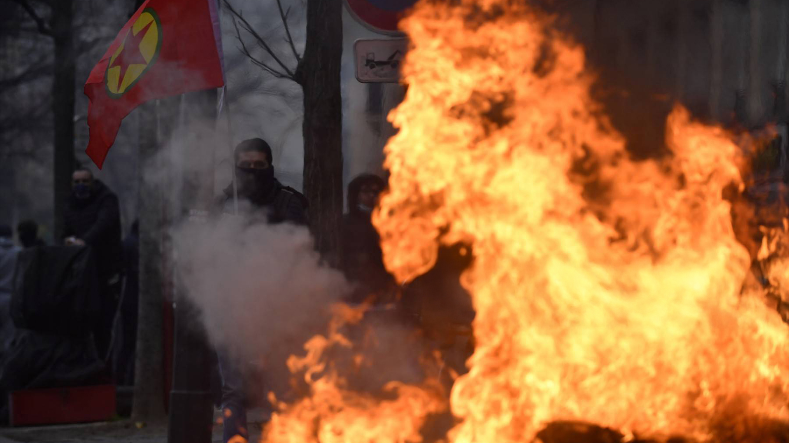 A protester holds a Kurdish workers party (PKK) flag behind a fire, at The Place de la Republique in Paris on Dec. 24, 2022.