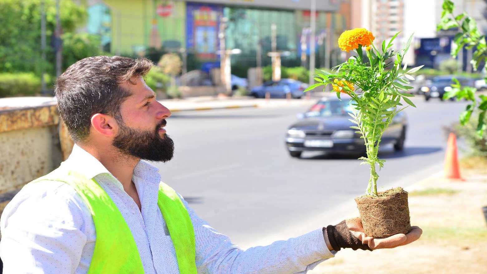 An Erbil Municipality employee holding a flower before he plants it, amid of a flower planting campaign in Erbil, June 2, 2025. (Photo: Kurdistan24)