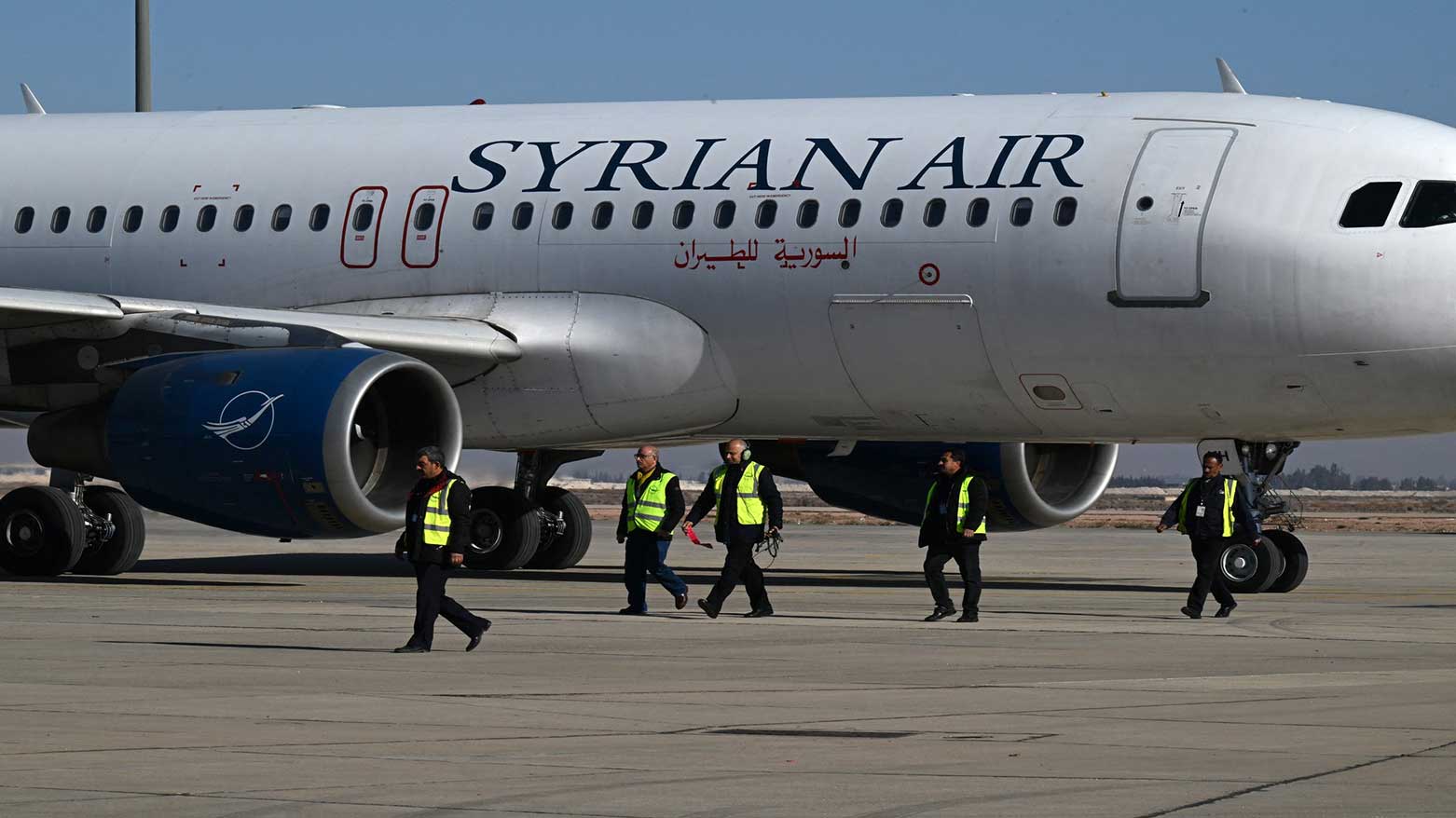 Ground personnel walk on the tarmac as a Syrian Air aircraft taxis ahead of take off to the city of Aleppo, on Dec. 18, 2024. (Photo: AFP)