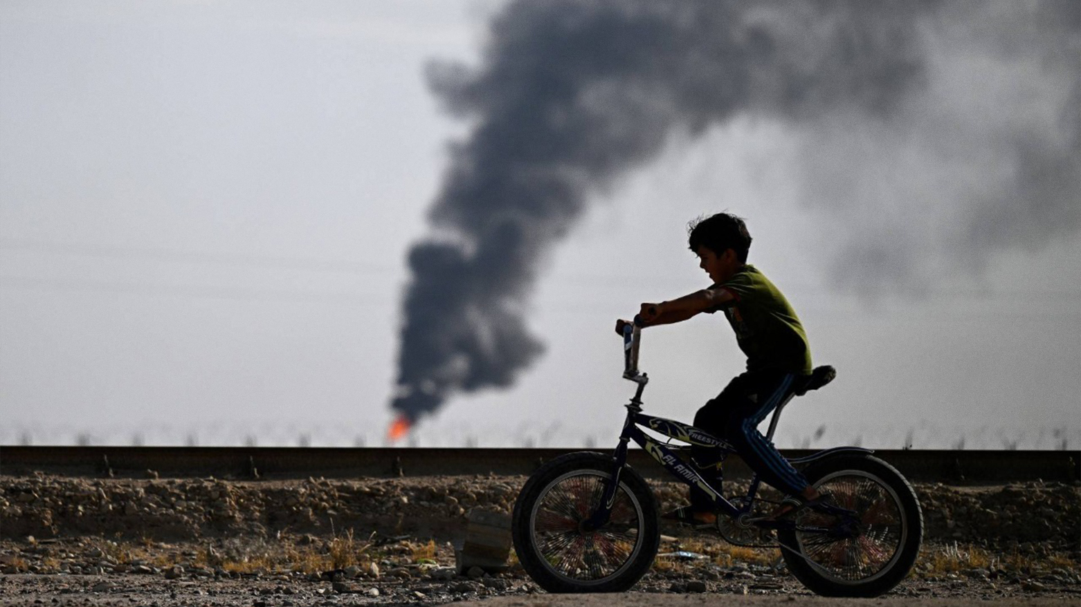 An Iraqi youth rides his bicycle near a flare stack in the Rumaila oil field near Iraq's southern port city of Basra on May 5, 2024. (Photo: AFP)