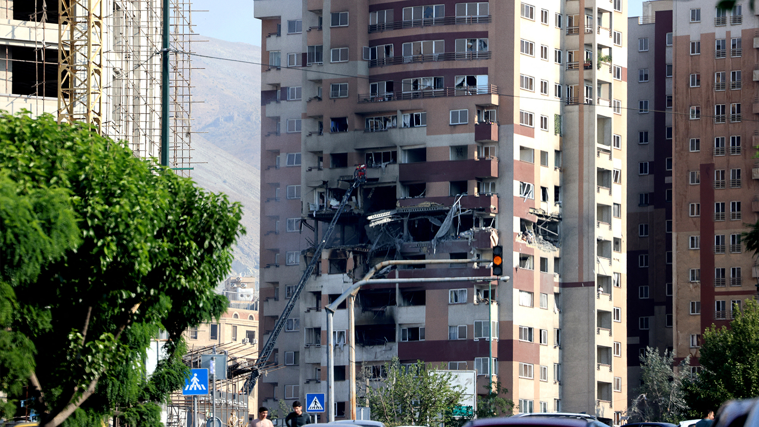 People walk past traffic in front of a building targeted by an Israeli strike in the Iranian capital Tehran on June 13, 2025. (Photo: AFP)