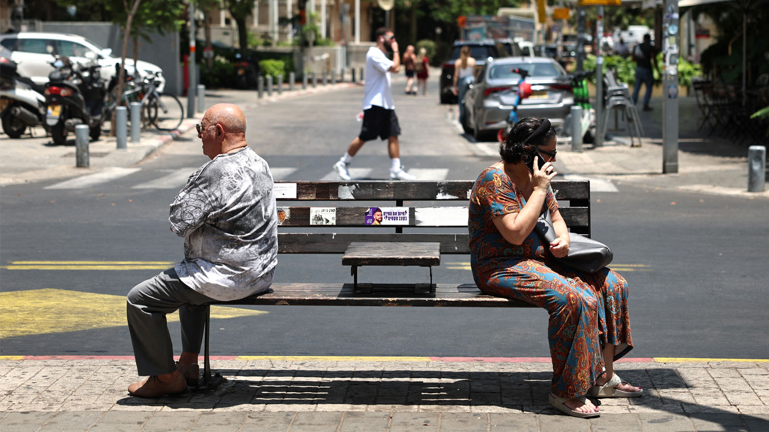 امرأة ورجل يقعدان على مقعد في شارع بتل أبيب (فرانس برس)