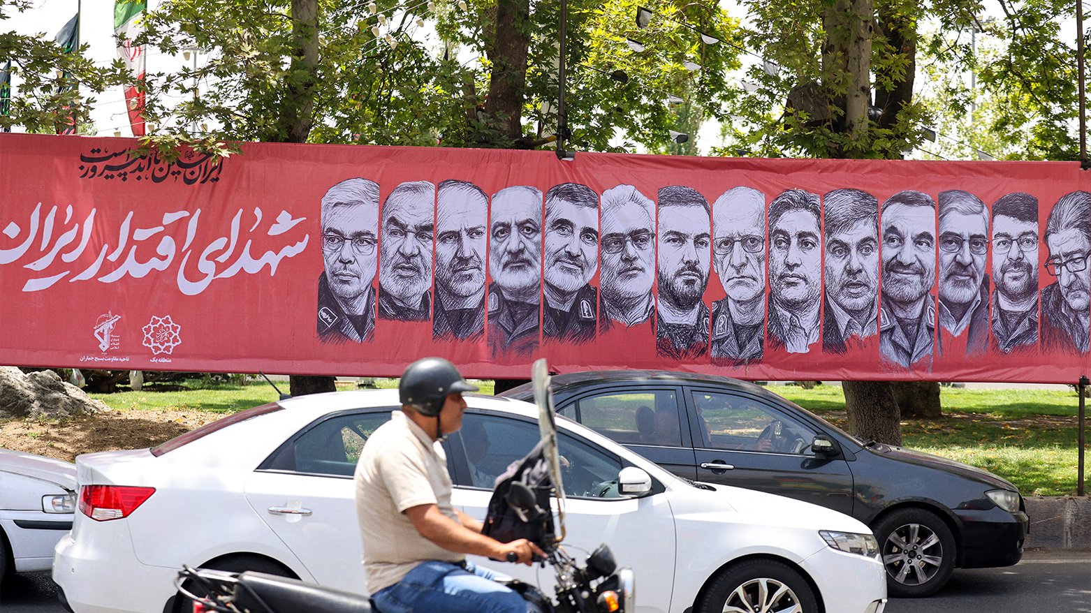 Traffic moves past a banner depicting Iranian commanders & scientists killed during the 12-day war. (Photo: AFP)