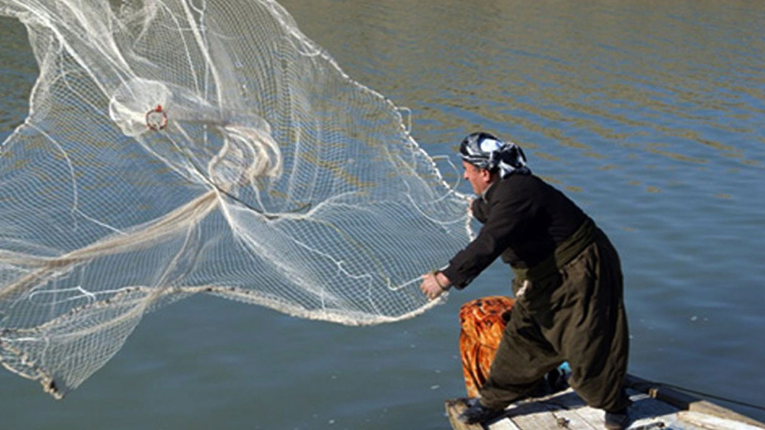 صياد أسماك يرمي بشباكه إلى المياه (تعبيرية)