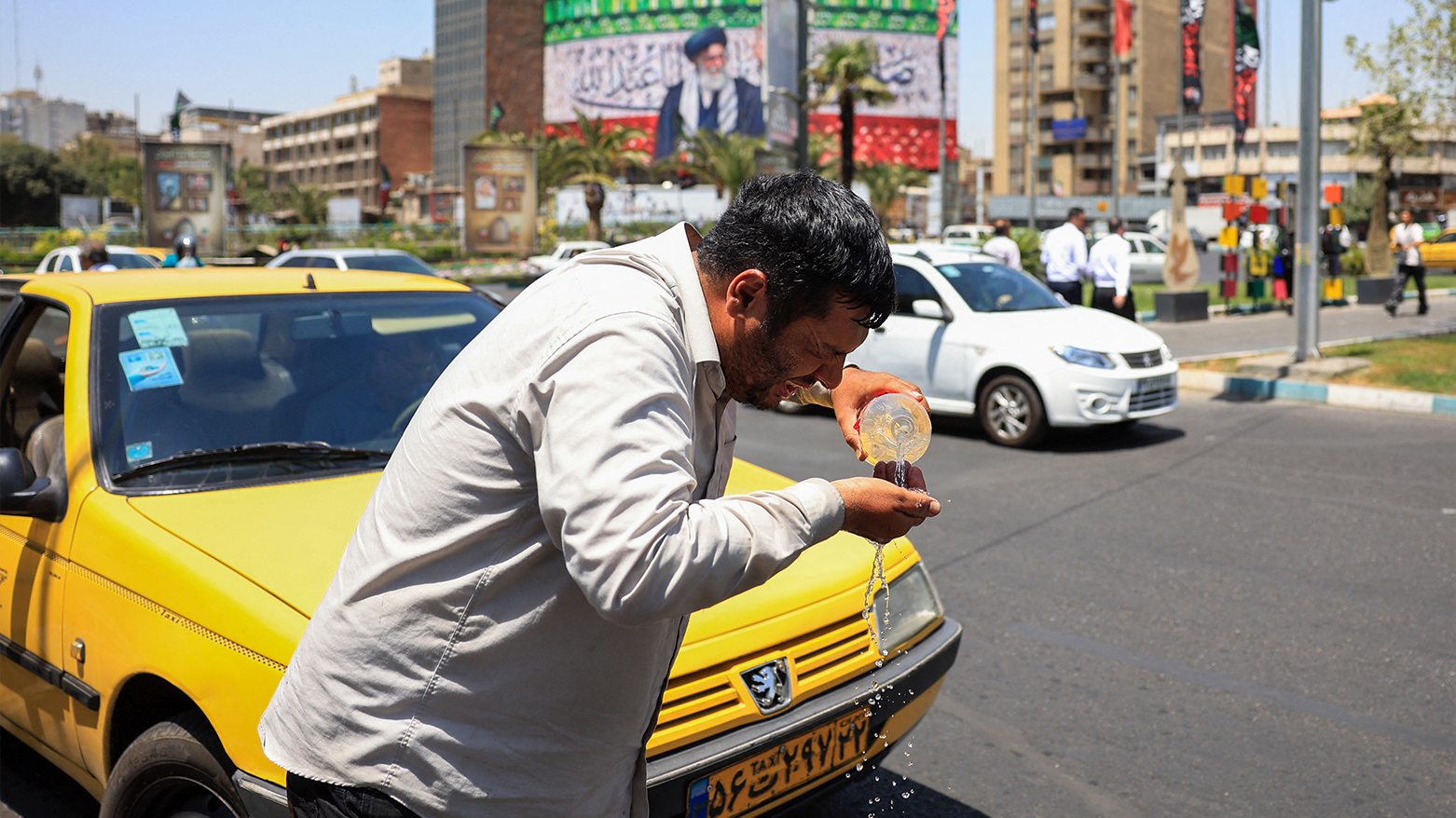 An Iranian taxi driver cools down by splashing water on his face on a street amid soaring temperatures in Tehran on July 22, 2025. (AFP)