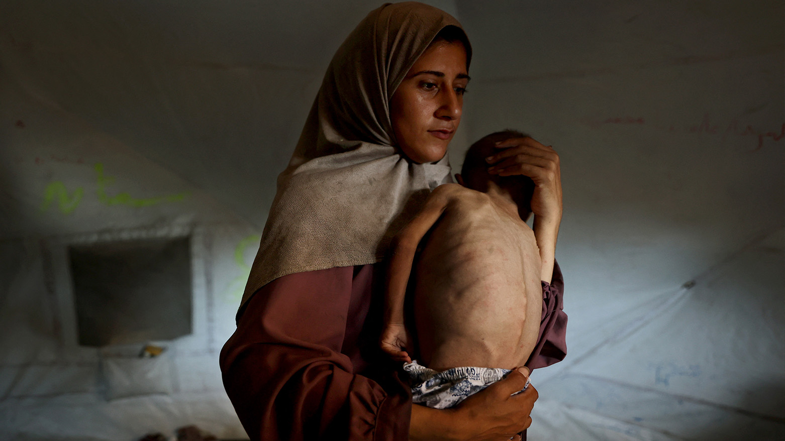 Hidaya, a 31-year-old Palestinian mother, carries her sick 18-month-old son Mohammed al-Mutawaq, inside their tent in west of Gaza City, on July 24, 2025. (Photo: AFP)
