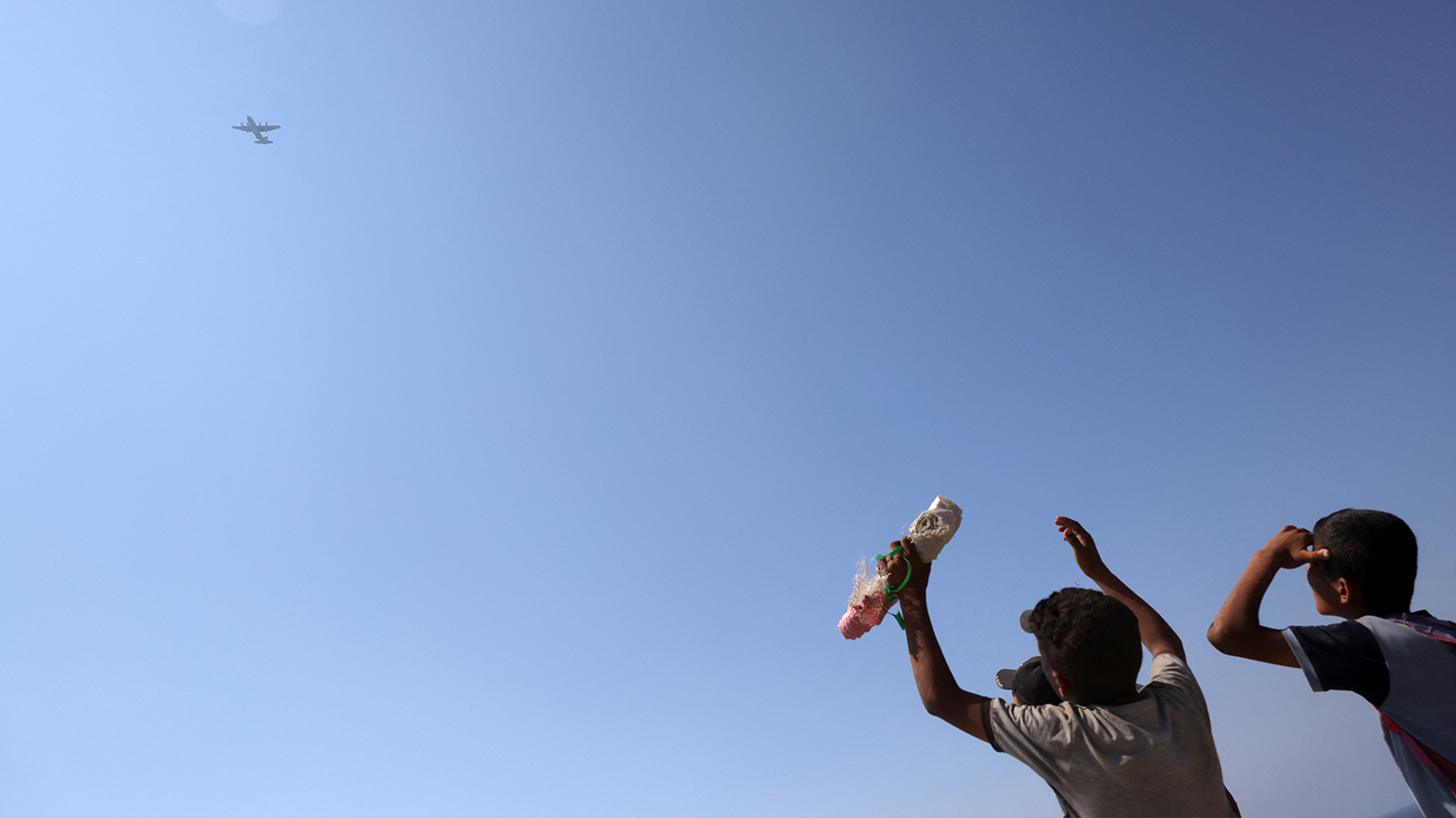 Children and youths gather as a C-130 Hercules military transport aircraft flies over during an aid drop on the northern Gaza Strip on Jul. 27, 2025. (Photo: AFP)