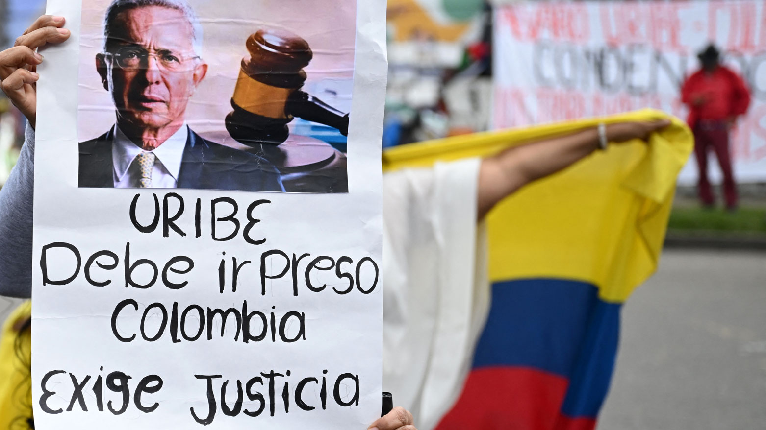 شخص يحمل لافتة ضد أوريبي خارج مجمع بالوكيماو القضائي في بوغوتا (فرانس برس)