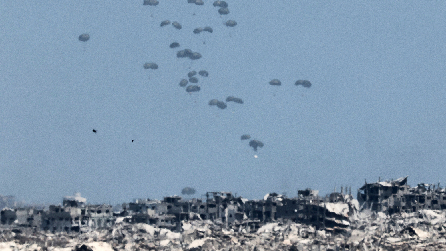 Aid is airdropped over Gaza amid ruins, seen from the Israeli border on August 1, 2025. (AFP)