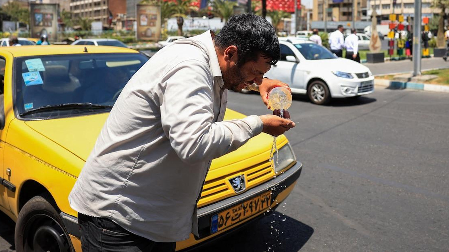An Iranian taxi driver cools down by splashing water on his face on a street amid soaring temperatures in Tehran, July 22, 2025. (Photo: AFP)