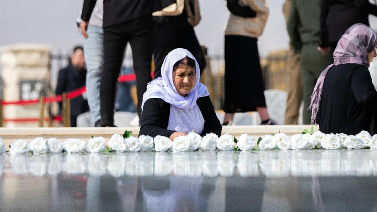 A Yazidi survivor places a white flower on the “Grave of Mothers” mass grave before its inaugural ceremony. (IOM)