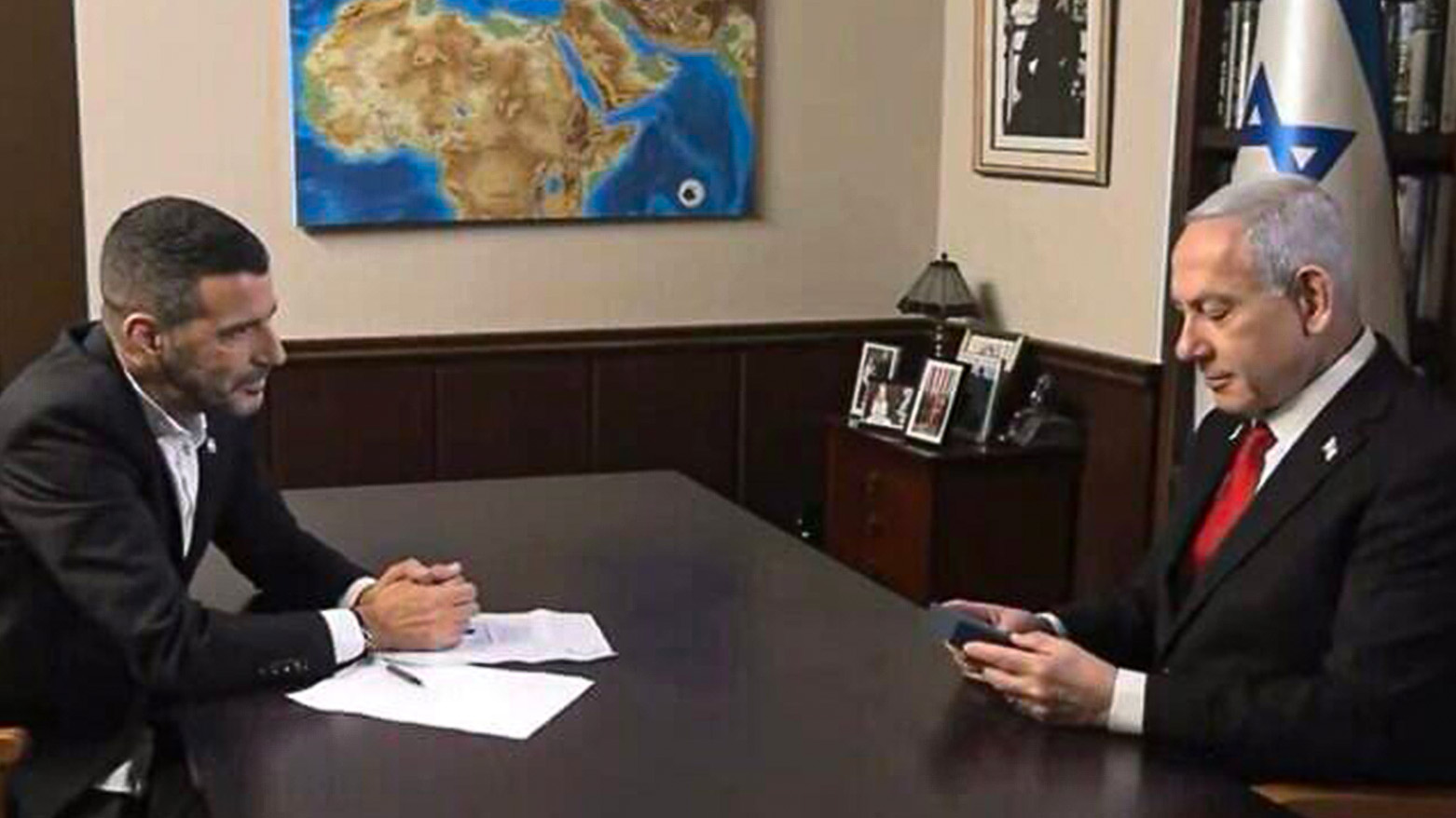 Prime Minister Benjamin Netanyahu looks at an amulet showing "a map of the Promised Land," given to him by his interviewer, Aug. 12, 2025. (Screenshot i24 news)
