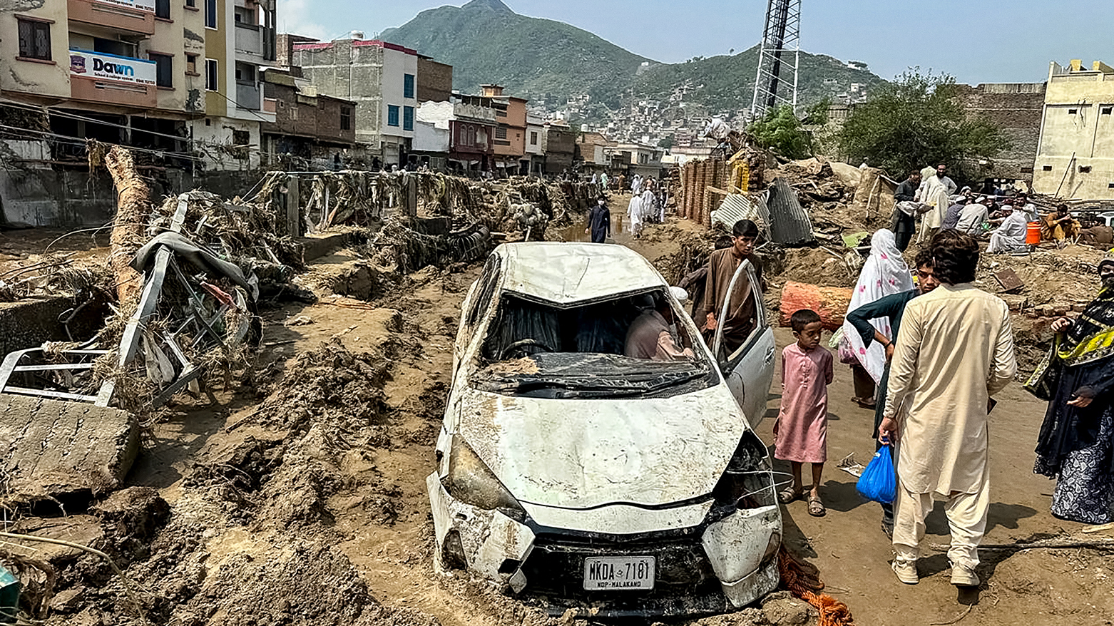 People gather near a damaged vehicle and scattered debris after the road washed out following a flash flood in Mingora. (AFP)