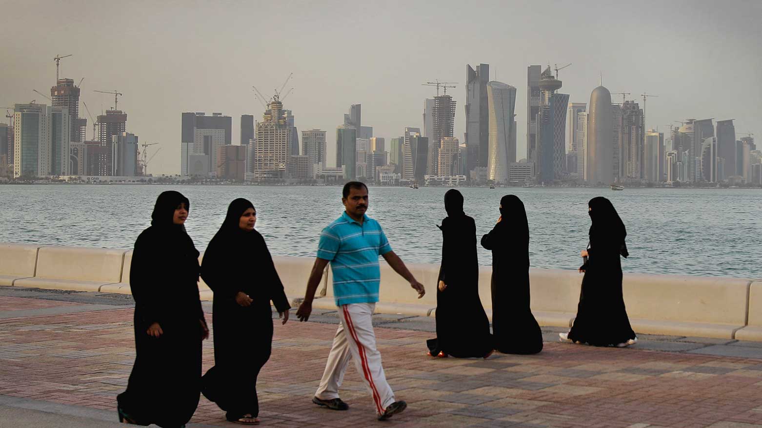 Qatari women and a man enjoy walking by the sea with downtown Doha in the background in Doha, Qatar. (Photo: AP)
