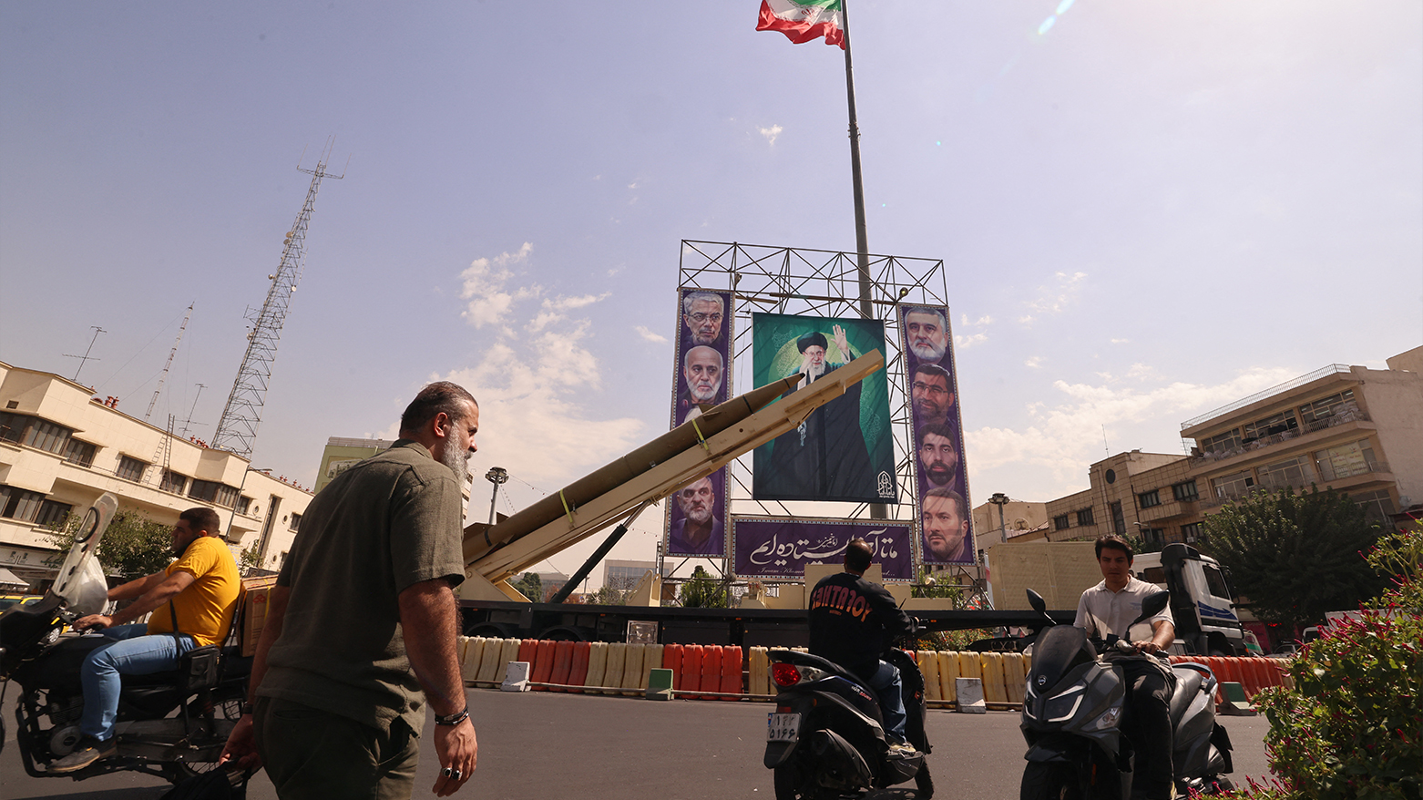 Iranians ride past a deactivated Kheibar Shekan missile beneath a portrait of Ayatollah Khamenei in Tehran’s Bahrestan Square, Sept. 27, 2025. (AFP)