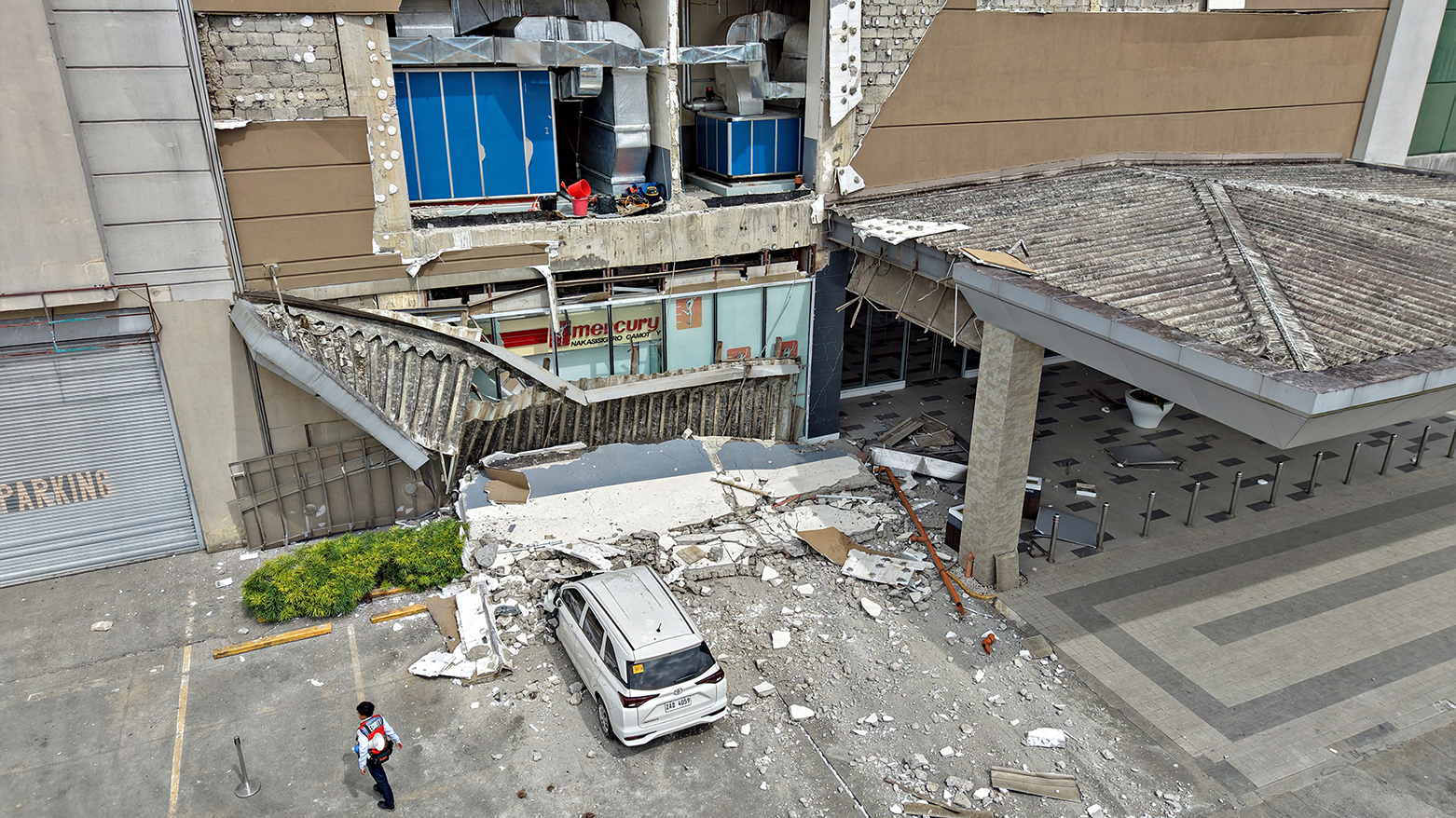 A security guard walks past a damaged wall and a car outside a mall in Butuan City, Philippines. (AFP)
