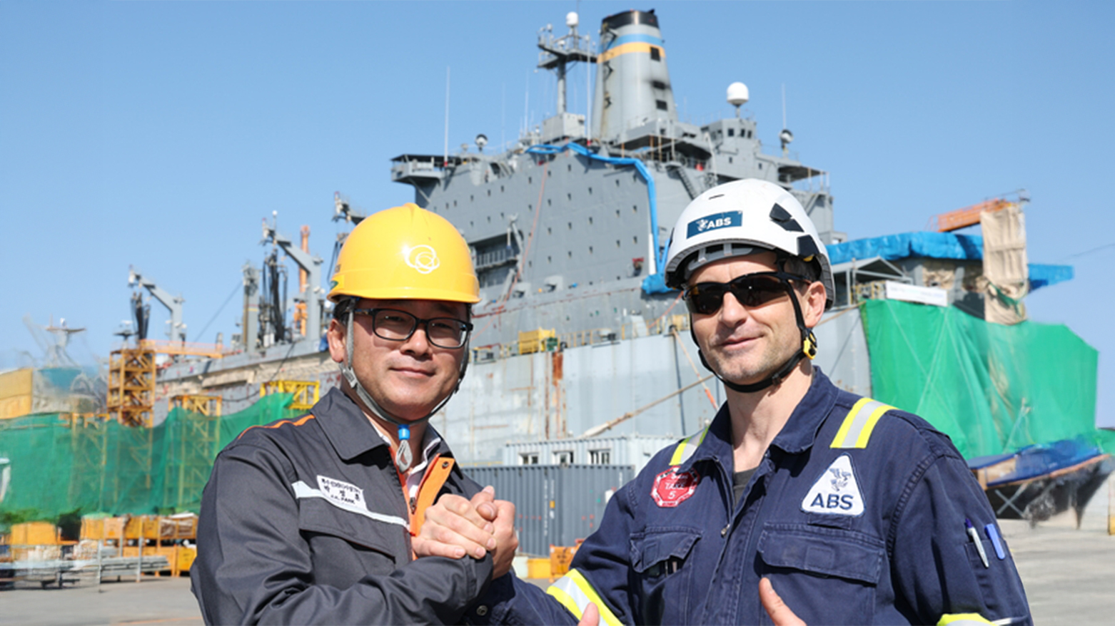 Park Jung-hoon, head of the MRO TF team of Hanwha Ocean Special Ship (L), Volodymyr Borovets, chief prosecutor of the American Association of Ships (ABS), holding hands at the shipyard. (Photo: Hanwha Ocean)