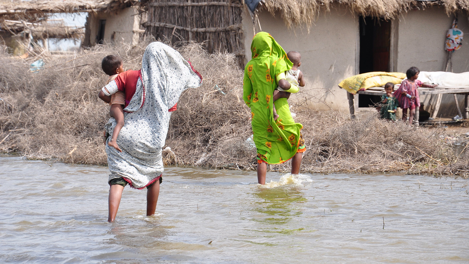 Two mothers holding their babies crossing a shallow river. (Photo: UN)