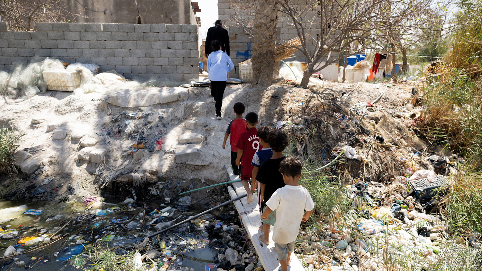 أطفال عائدين إلى منازلهم عبر مجرى مائي ملوث في قرية المشعب في الأهوار شمال البصرة (فرانس برس)