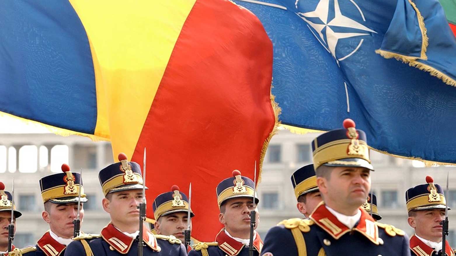 Romanian soldiers stand at attention backdropped by the Romanian, (L), and the NATO flag during the ceremony to mark the accession of Romania to NATO in Bucharest, April 2, 2004.