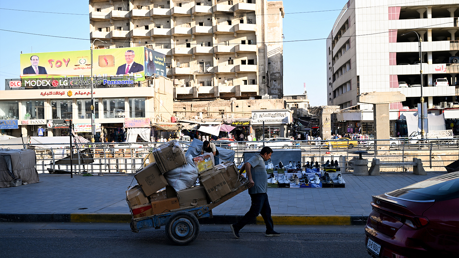 A man pulls a cart loaded with boxes past campaign billboards ahead of Iraq's elections in Basra on Nov.1, 2025. (AFP)