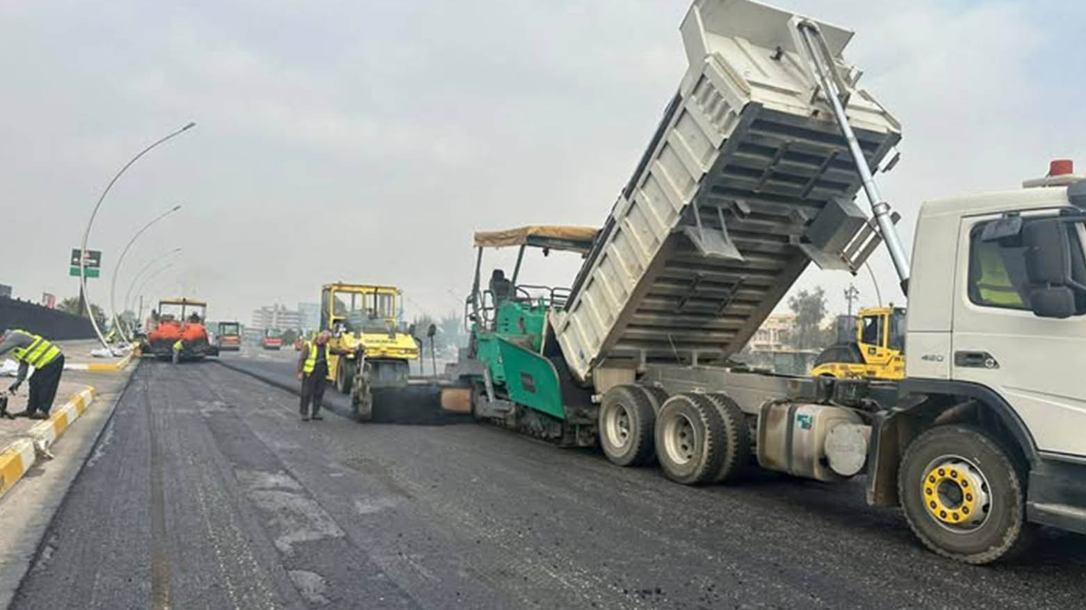 Workers resurfacing a street, with a dump truck unloading asphalt into a paving machine in the newly laid road surface in Erbil. (Photo: KRG)