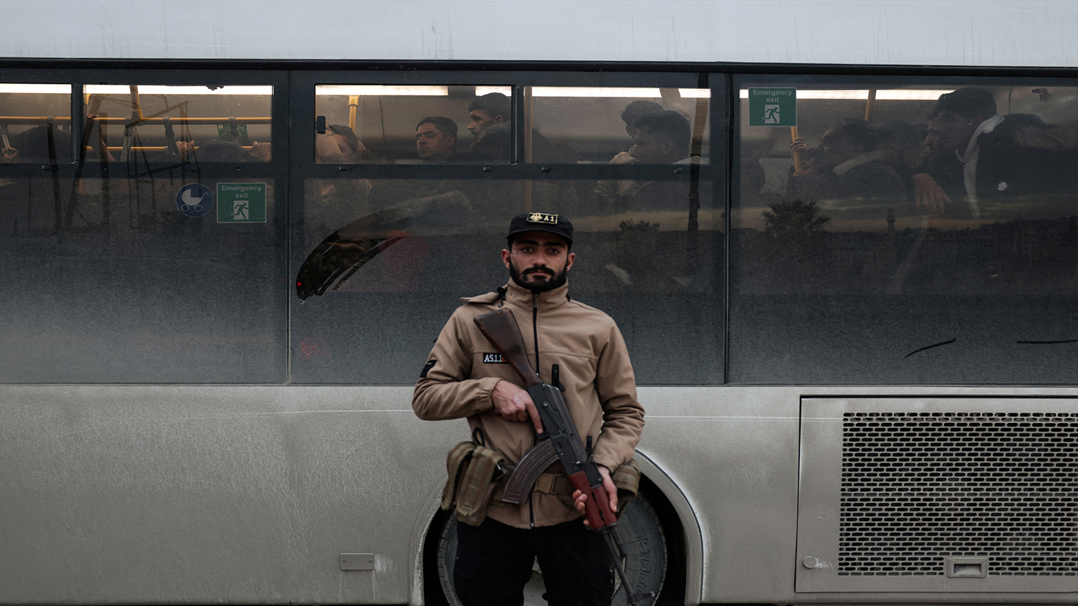 A Syrian government officer stands guard over detained Kurds being escorted to detention centers, in the city of Aleppo, on Jan. 10, 2026. (AFP)