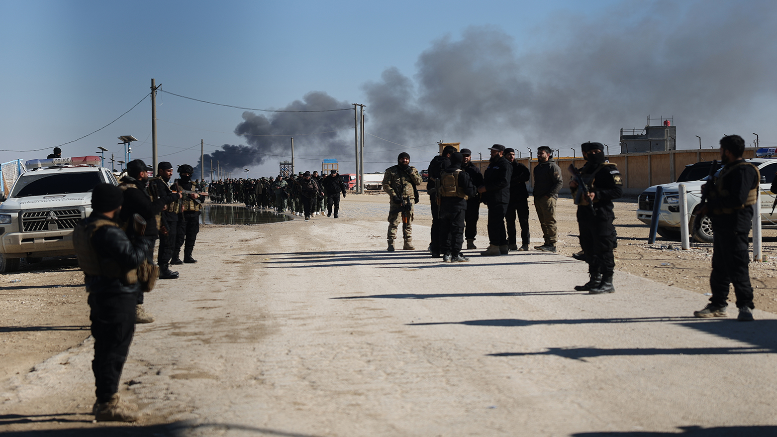 Syrian government forces patrol inside the al-Hol camp as smoke rises from an arms depot explosion in northeastern Syria's Hasakeh province, Jan. 21, 2026. (AP)
