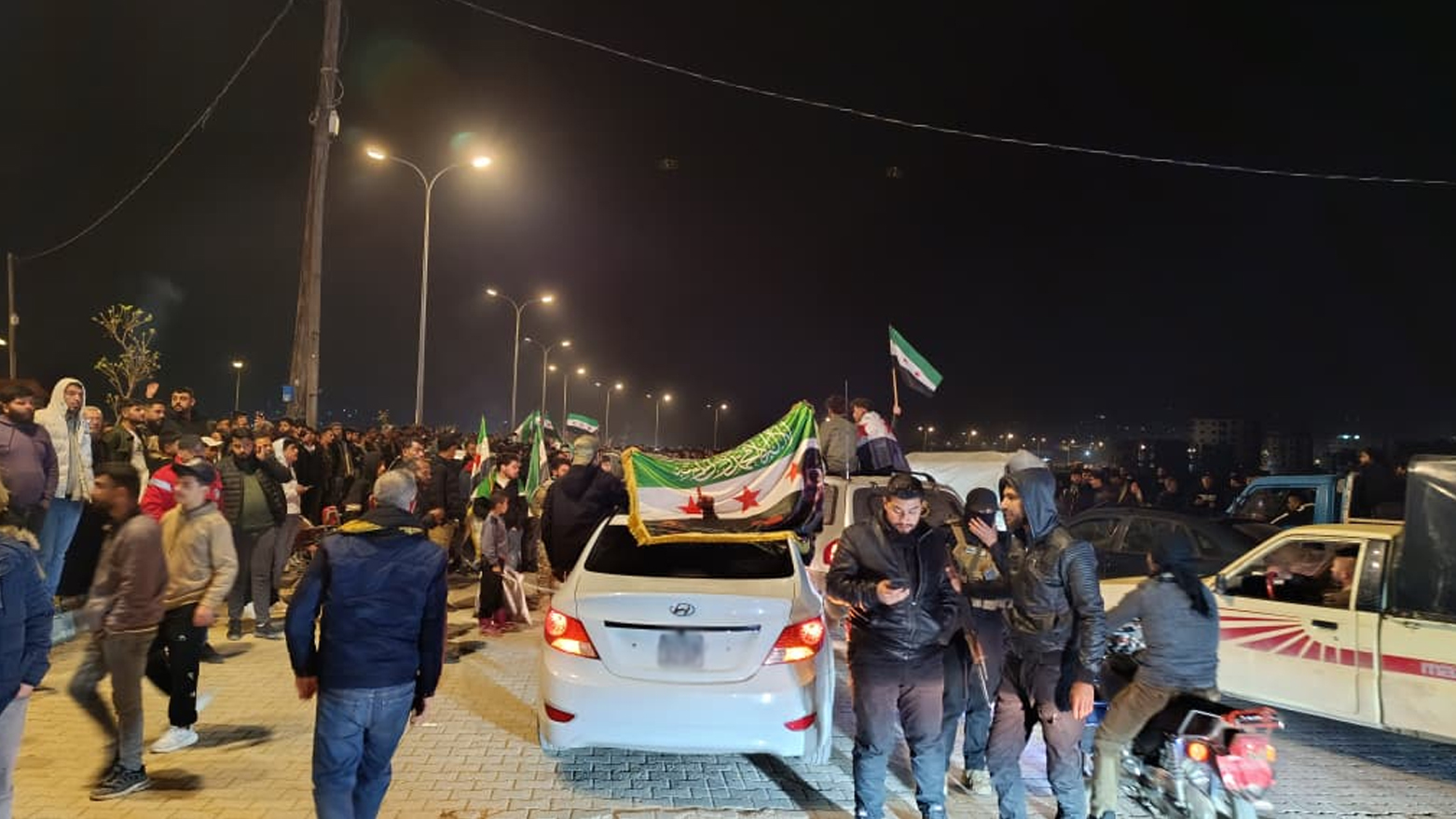 Settlers chant racist slogans against the Kurds and raise the Syrian flag with slogans of monotheism written on it in front of the Kurds who are receiving the Afrini IDPs, in front of the security forces. (Photo: Handed to Kurdistan24)