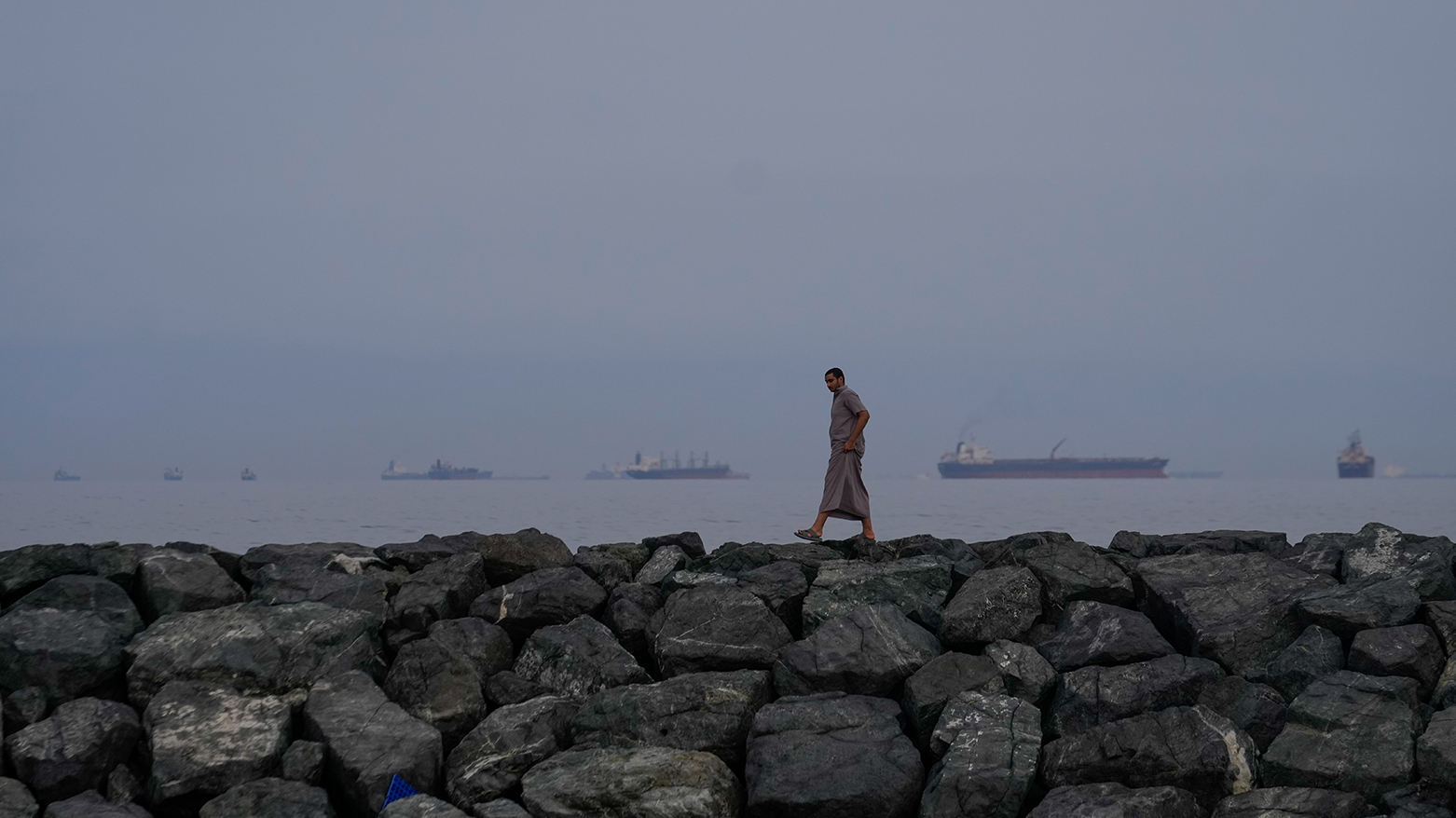 A man walks along the shore as oil tankers and cargo ships line up in the Strait of Hormuz. (AP)