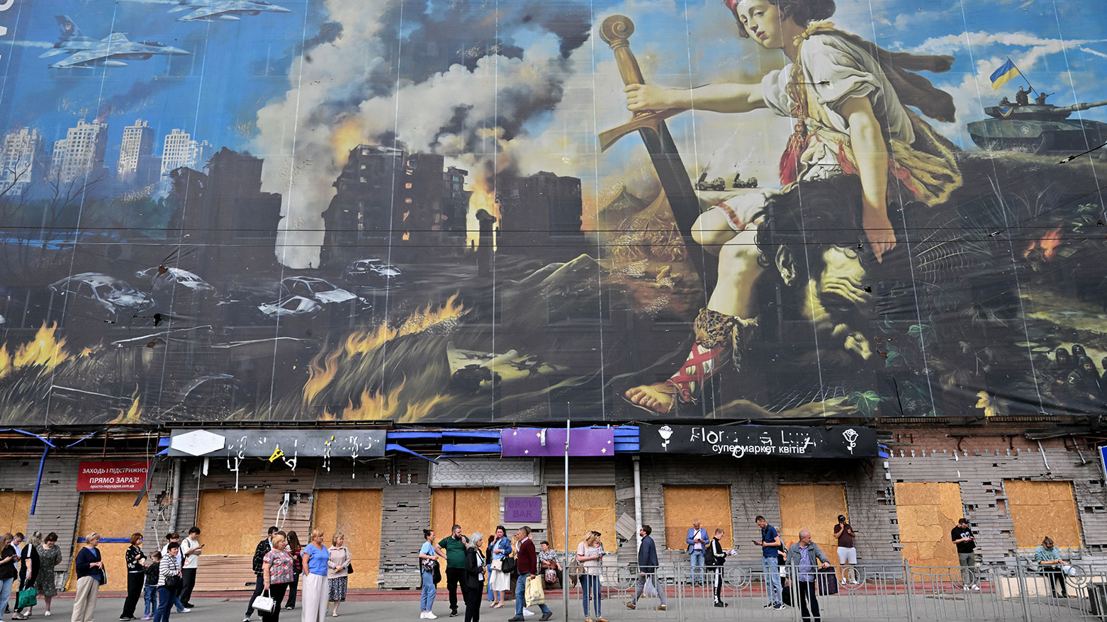 People wait at a Kyiv bus stop beside a giant hoarding concealing strike damage. (Photo: AFP)