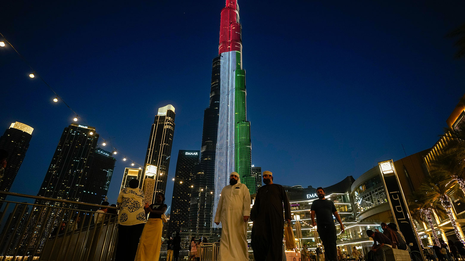 People walk as Burj Khalifa, the world's tallest building, is illuminated with the UAE national flag colors Dubai, UAE, May 6, 2026. (AP)
