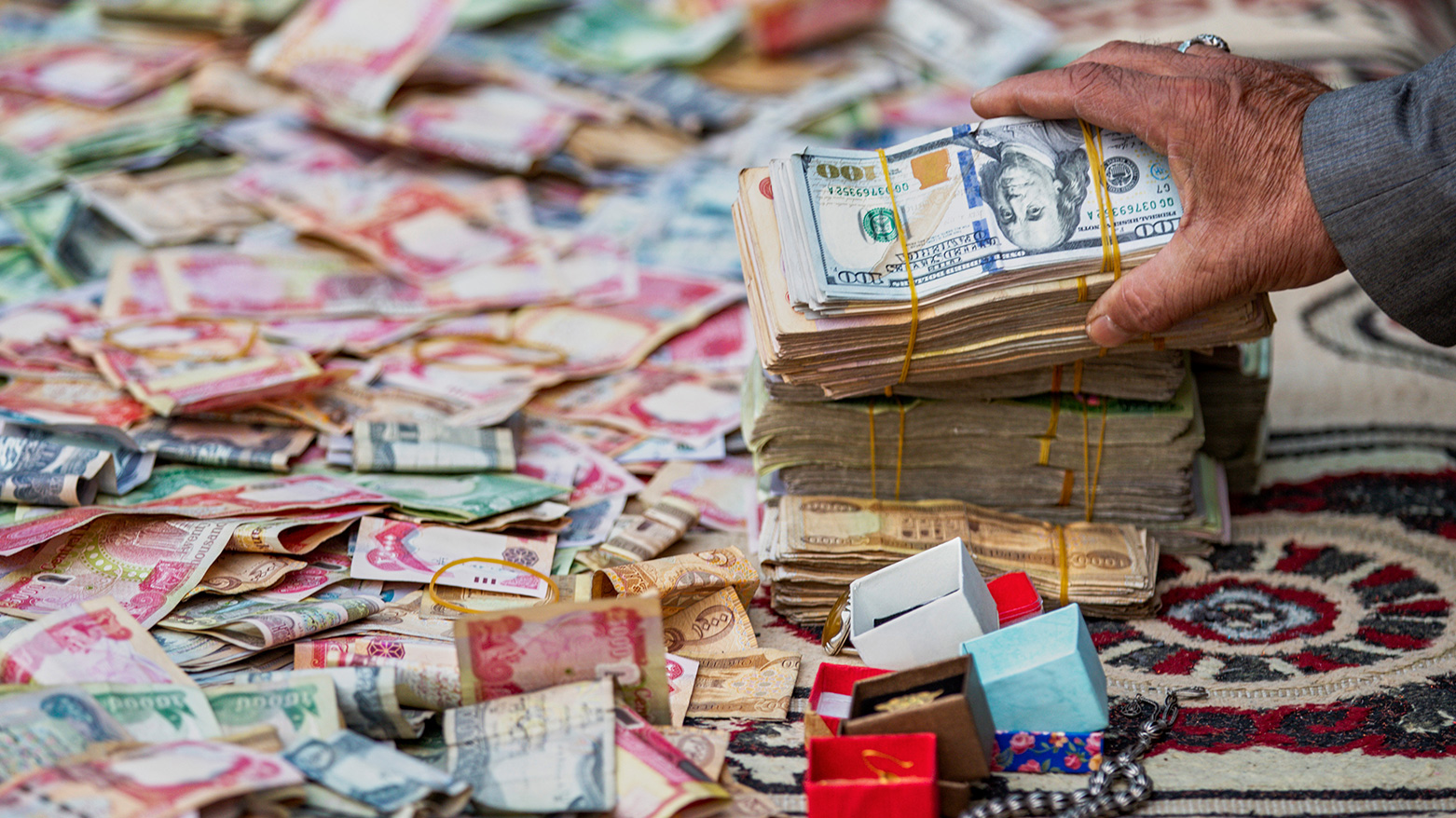 Stacks of Iraqi dinars and US dollars spread across a traditional carpet. (AP)