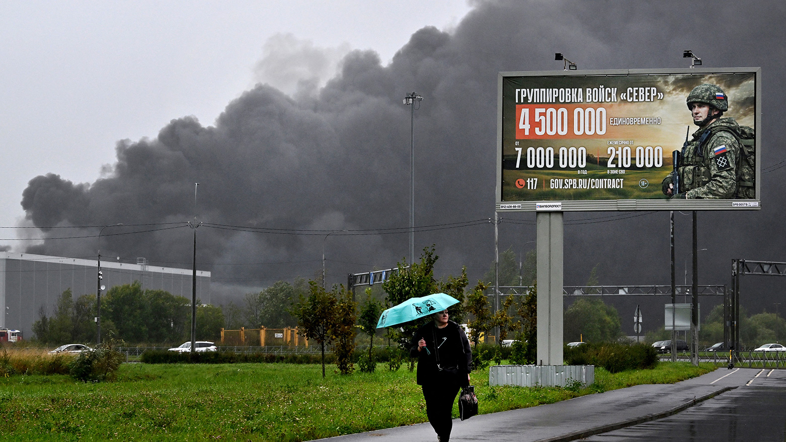 Smoke rises over a logistics center in Kolpino, outside Saint Petersburg behind a billboard promoting contract army service after being hit by Ukrainian drones early on Aug. 23, 2026. (AFP)