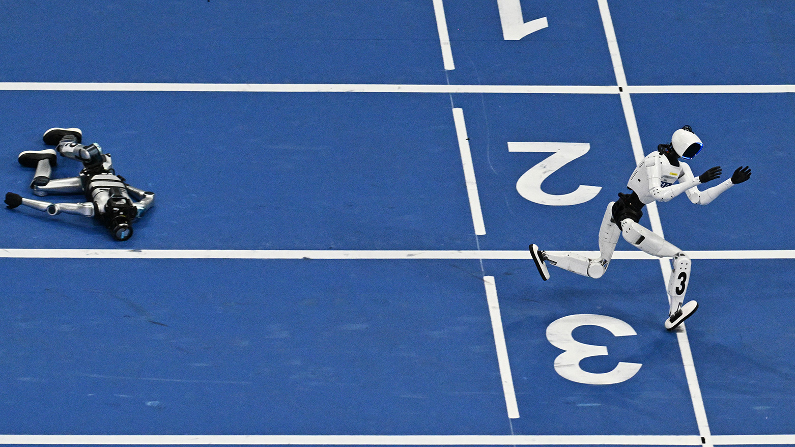 A humanoid robot runs past a fallen competitor in the 400-meter race on the second day of the 2nd World Humanoid Robot Games in Beijing on August 23, 2026. (Photo by Pedro PARDO / AFP)
