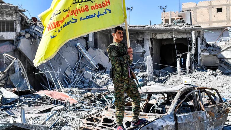 A member of the Syrian Democratic Forces (SDF) holds up the group's flag at the iconic Al-Naim square in Raqqa, Syria, during the celebration of Raqqa's liberation, Oct. 17, 2017. (Photo: Bulent Kilic, AFP/Getty Images).